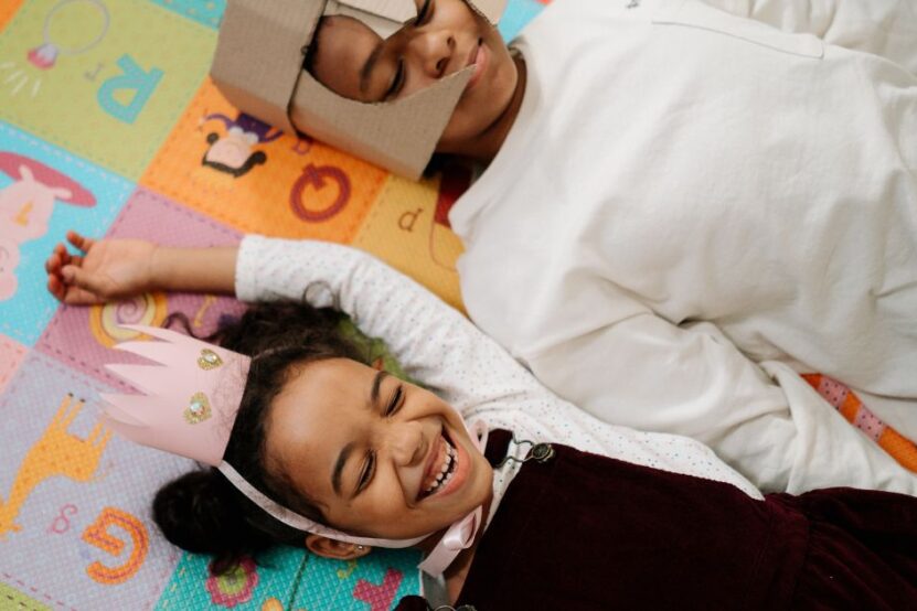 Picture shows two young children laying on their backs smiling