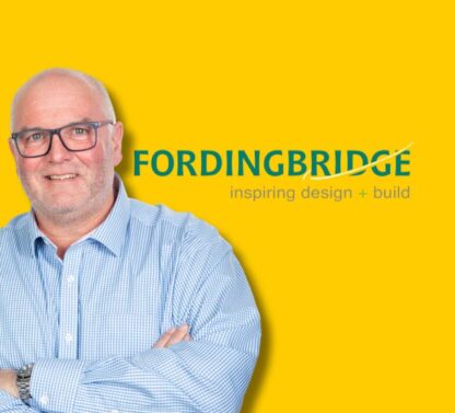 Picture shows Steve Toone standing with arms crossed on a yellow background with the company logo (fordingbridge) to his right.