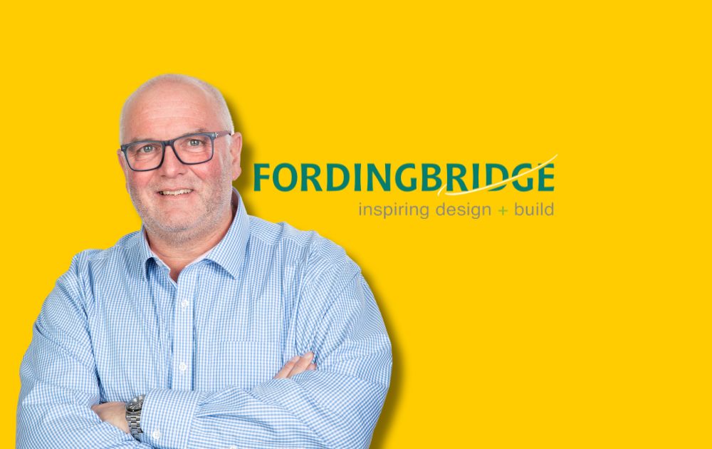 Picture shows Steve Toone standing with arms crossed on a yellow background with the company logo (fordingbridge) to his right.
