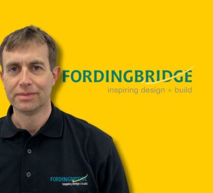 Picture Shows Hunter, the new factory manager at Fordingbridge looking straight out standing in front of a plan yellow background next to the Fordingbridge logo