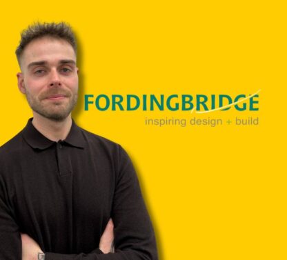 Picture shows Tony Merriman standing in front of a plain yellow background with the Fordingbridge logo to his righthand side
