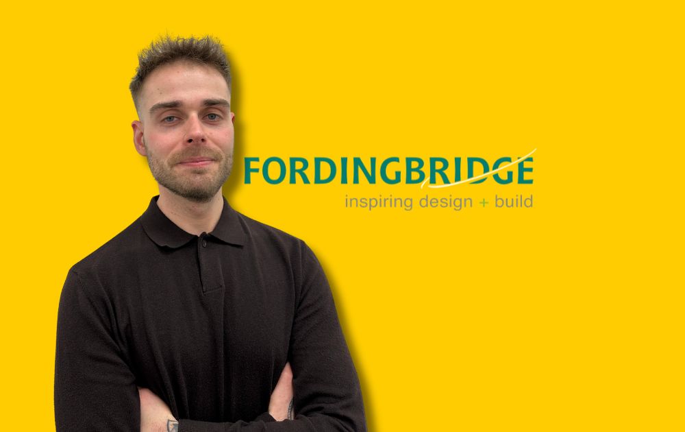 Picture shows Tony Merriman standing in front of a plain yellow background with the Fordingbridge logo to his righthand side