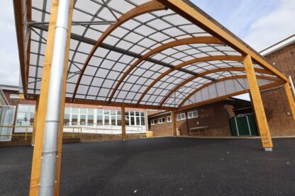 Wooden canopy with a curved roof outside a school building.