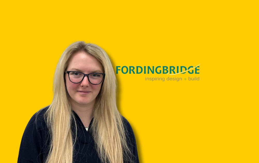 Picture shows Olivia LeGon standing in front of a yellow wall with the fordinbridge logo to her right