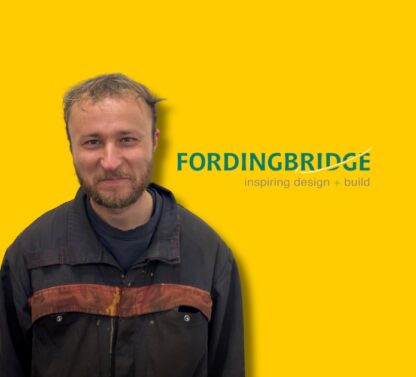 Picture show Harry the new Welder at Fordingbridge just smiling and standing in front of a yellow background.