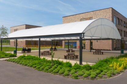 Large contemporary school dining canopy at Manor Drive Academy in Peterborough, providing a covered outdoor seating area with picnic benches beside a modern brick school building.