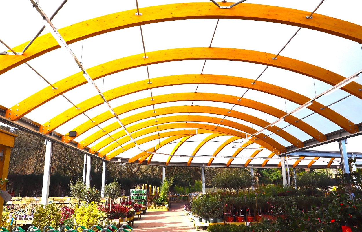 All-weather garden centre canopy with curved timber beams covering plant displays and browsing area
