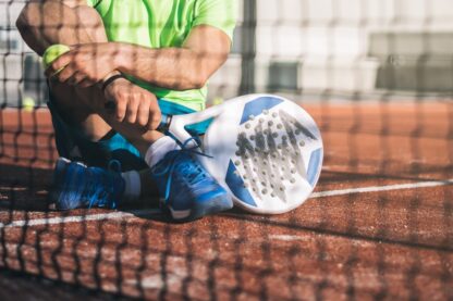 Close-up of padel player resting on court with racket and ball beside the net