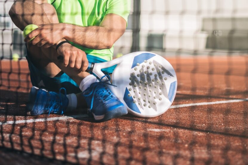 Close-up of padel player resting on court with racket and ball beside the net