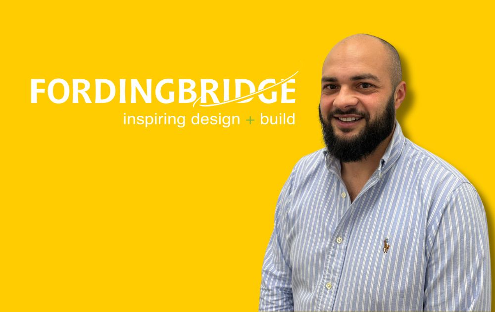 Man smiling in front of a yellow Fordingbridge background with “inspiring design + build” text, wearing a striped shirt.