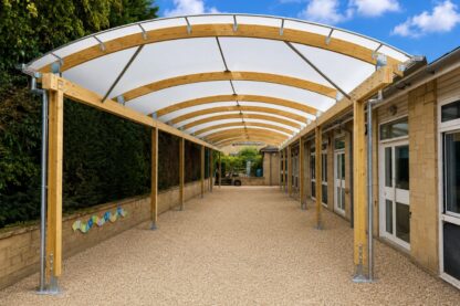 Barrel-vaulted timber school canopy at St David’s C of E Primary School, creating a covered outdoor learning space alongside the classrooms.